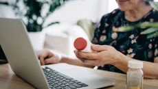 A close up of a person holding a pill bottle while using a laptop A close up of a person holding a pill bottle while using a laptop
