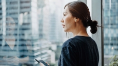 A young woman holding a smartphone and looking out a window. A young woman holding a smartphone and looking out a window.