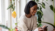A young woman sitting near a window using a smartphone A young woman sitting near a window using a smartphone