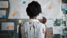 A woman standing with her back to the camera before a wall covered in planning documents and post-it notes A woman standing with her back to the camera before a wall covered in planning documents and post-it notes
