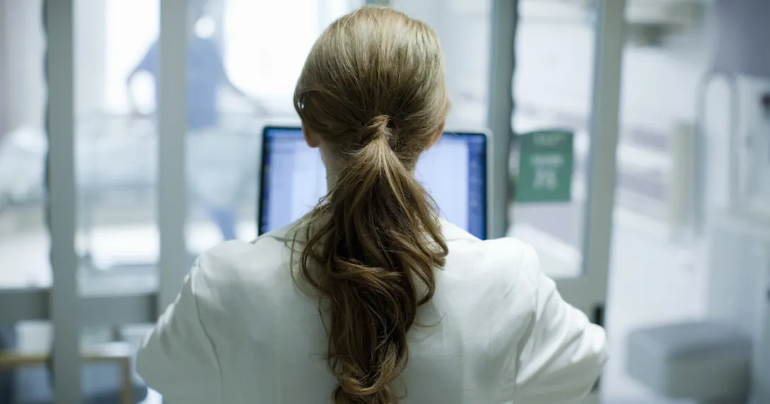 Healthcare provider standing with their back facing the camera in a clinic Healthcare provider standing with their back facing the camera in a clinic