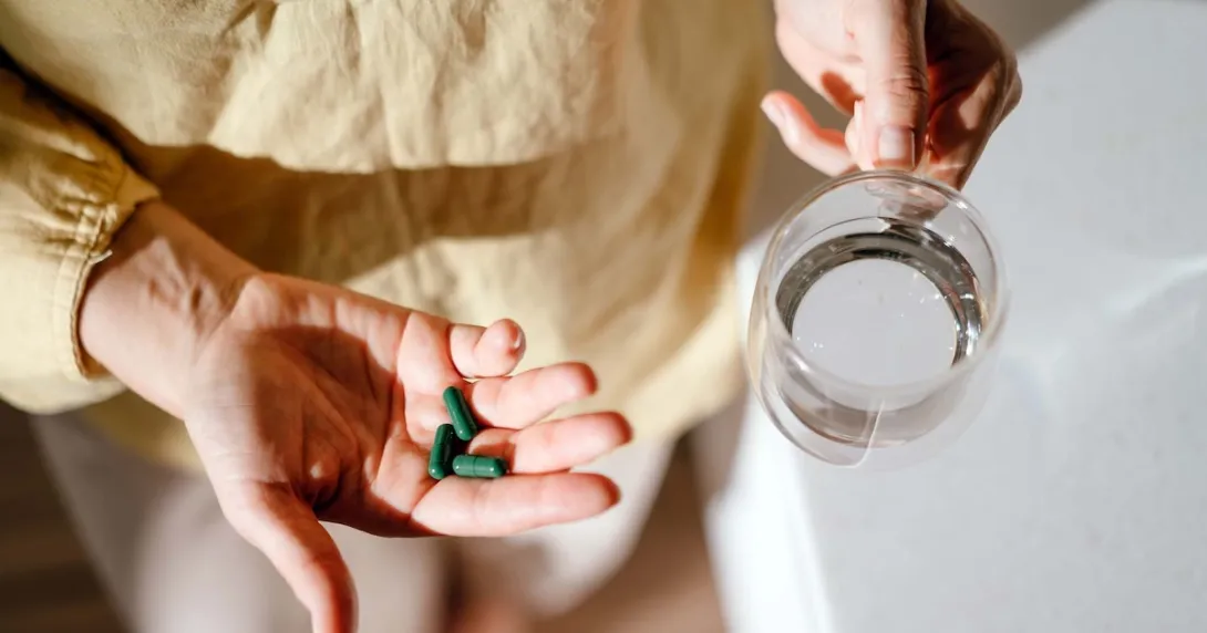 Person holding pills and a glass of water Person holding pills and a glass of water