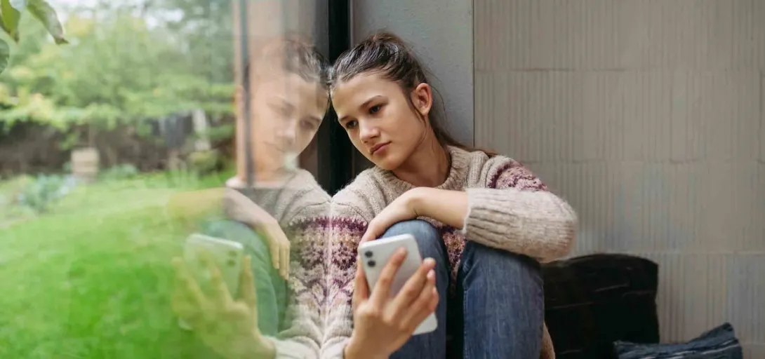 Person sitting by a window while holding a phone Person sitting by a window while holding a phone