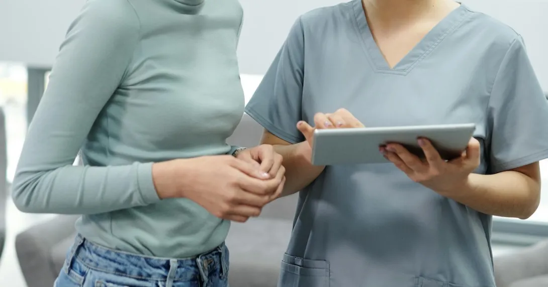 A nurse holding a digital tablet assisting a patient with their records