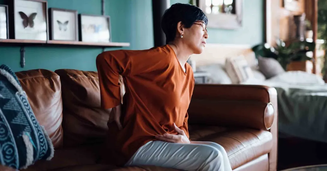 Person sitting on a couch while holding their back and their stomach