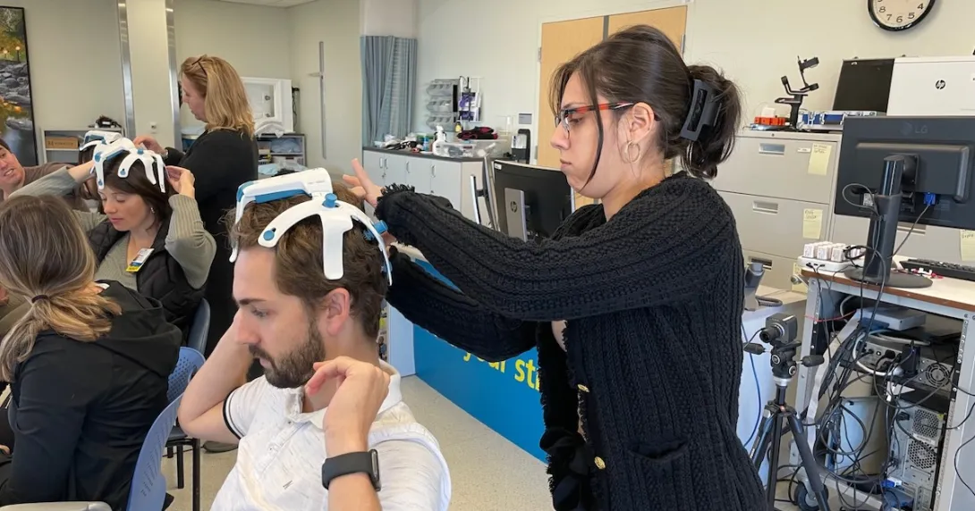 A therapist-in-training putting on the SynPhNe device on a volunteer's head A therapist-in-training putting on the SynPhNe device on a volunteer's head
