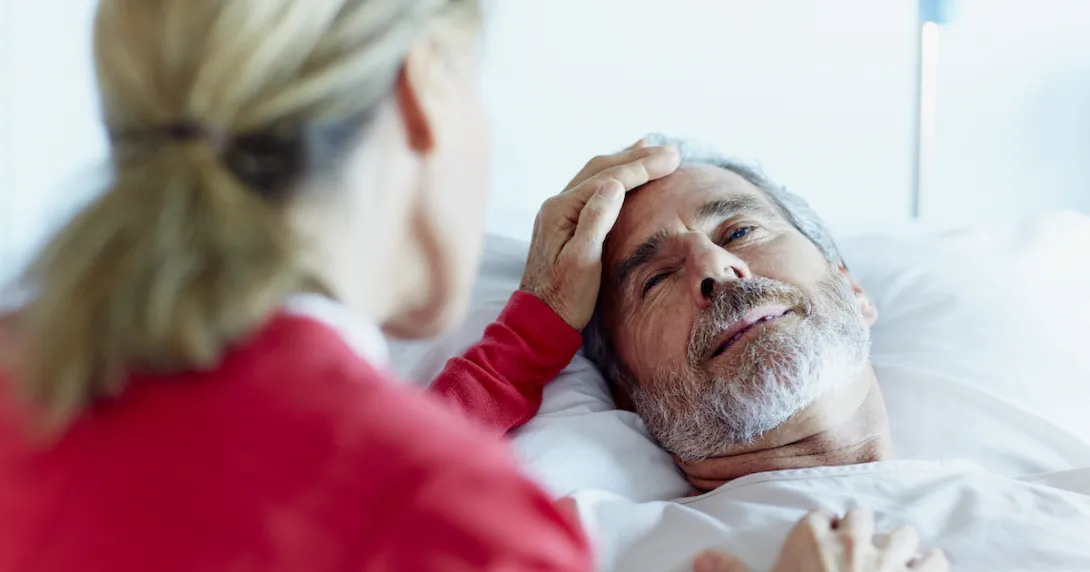 Person in a red shirt sitting next to someone in a hospital gown lying in a bed Person in a red shirt sitting next to someone in a hospital gown lying in a bed