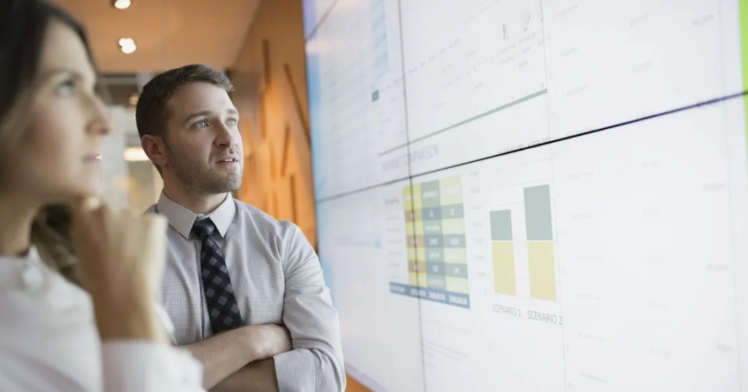 Two people standing in front of a large white board that has graphs on it