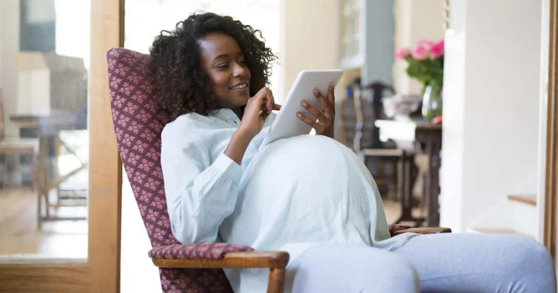 A pregnant person sitting in a chair while looking at a tablet A pregnant person sitting in a chair while looking at a tablet