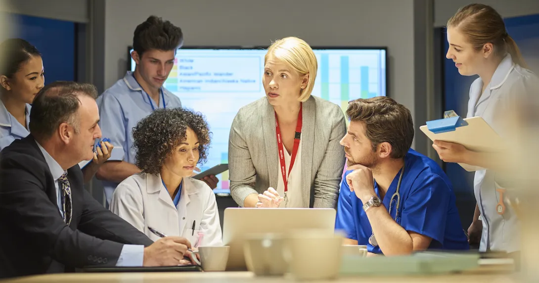 People sitting and standing around a table looking at a computer People sitting and standing around a table looking at a computer