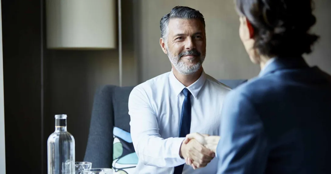 Two people sitting across from each other at a desk shaking hands Two people sitting across from each other at a desk shaking hands