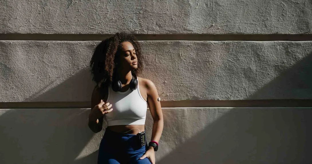 Person wearing a glucose monitor while standing against a wall Person wearing a glucose monitor while standing against a wall