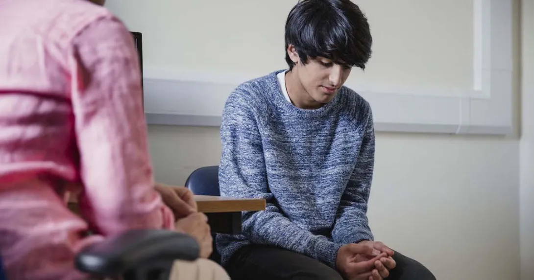 Two people sitting in a room, one with their head down Two people sitting in a room, one with their head down