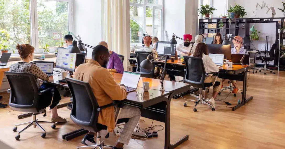 Numerous people sitting at large desks in a big room Numerous people sitting at large desks in a big room