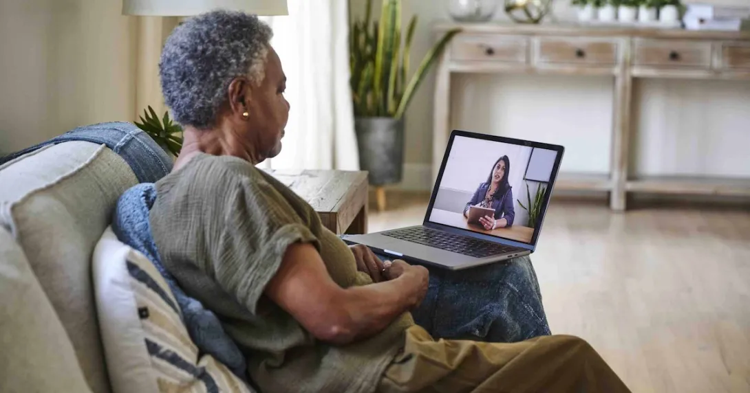 Person sitting on their couch in their home while talking to a telehealth provider on their computer Person sitting on their couch in their home while talking to a telehealth provider on their computer