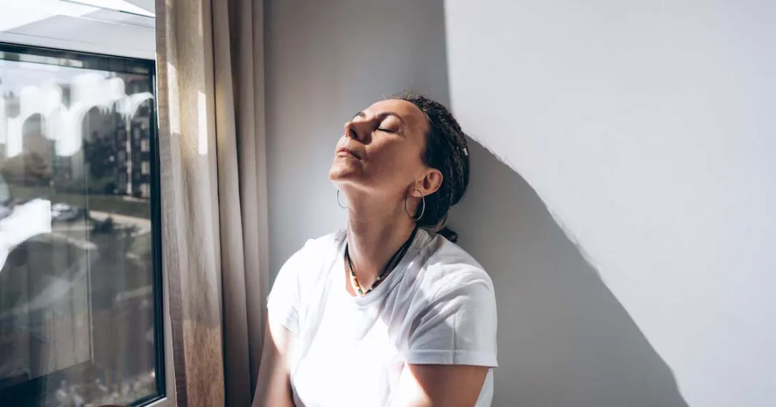 Person sitting next to a window with their eyes closed and their chin raised