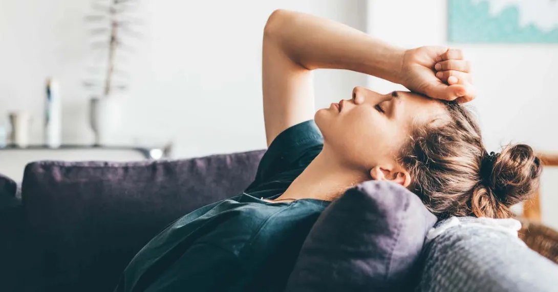 Person lying on a couch with their hand on their forehead with their eyes closed Person lying on a couch with their hand on their forehead with their eyes closed