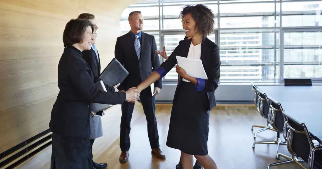 Four business people standing in a room with two of them shaking hands Four business people standing in a room with two of them shaking hands