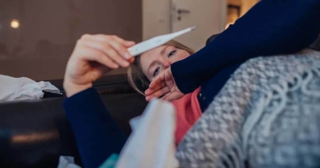 Person lying on their couch looking at a thermometer Person lying on their couch looking at a thermometer