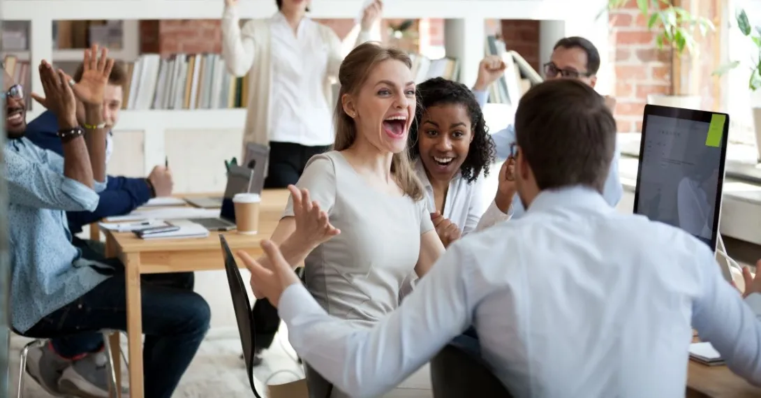 Three people with arms raised celebrating around computer monitor Three people with arms raised celebrating around computer monitor