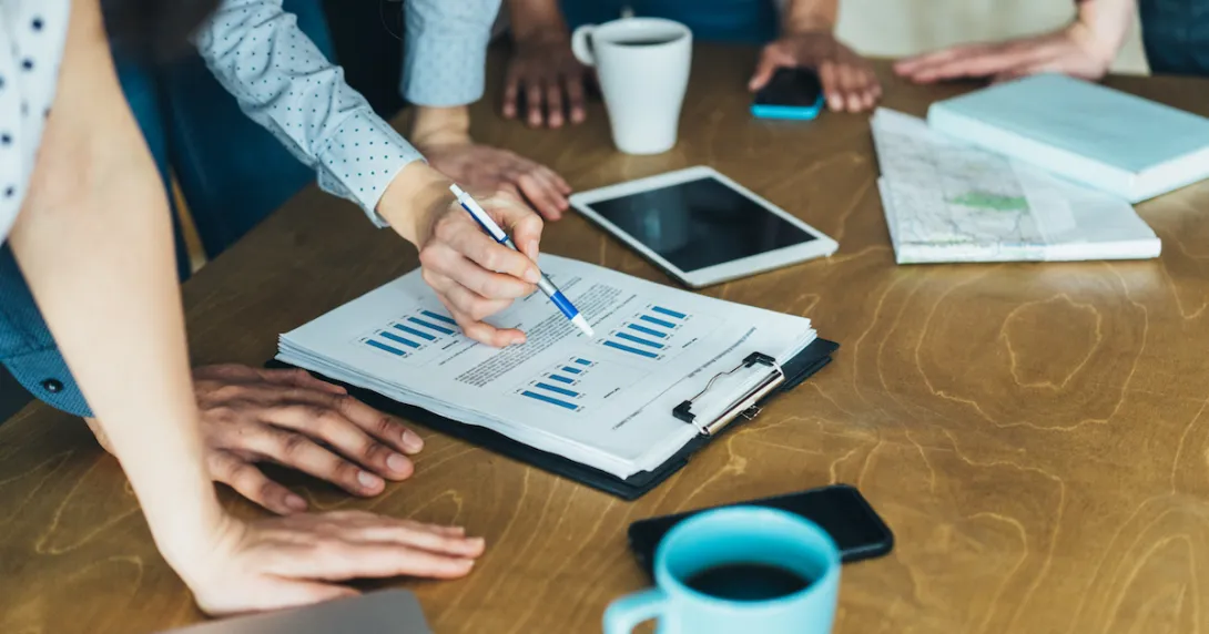 People standing around a table looking at a document People standing around a table looking at a document