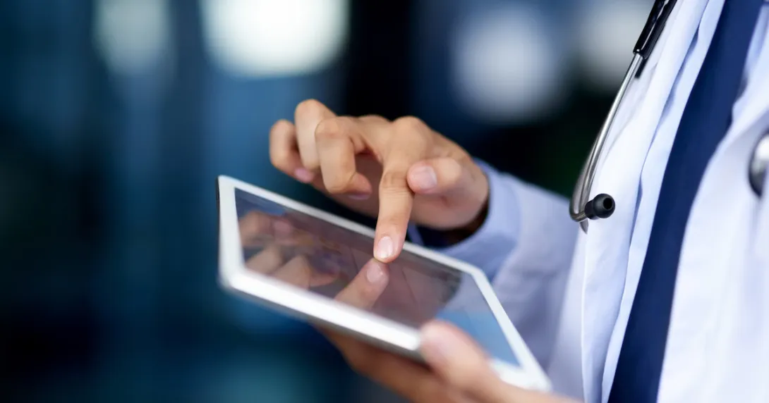 Healthcare provider using a tablet while wearing a white coat and stethoscope Healthcare provider using a tablet while wearing a white coat and stethoscope