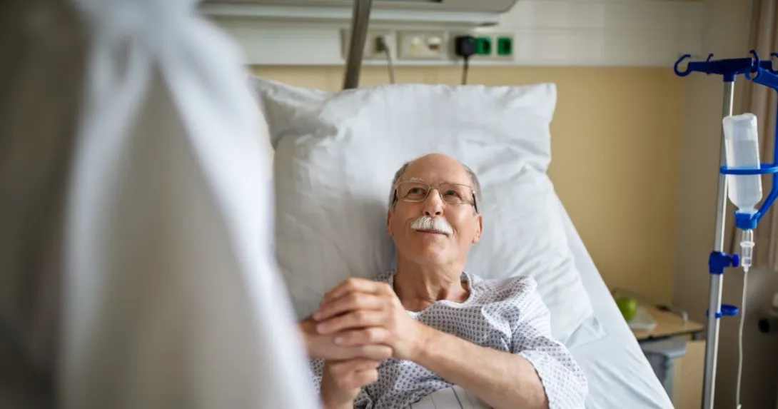 person in hospital bed holds hand of person in white lab coat