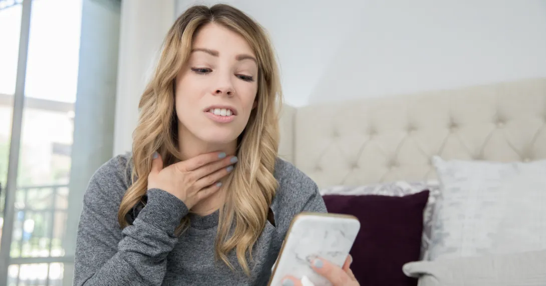 Person on a cellphone holding their throat