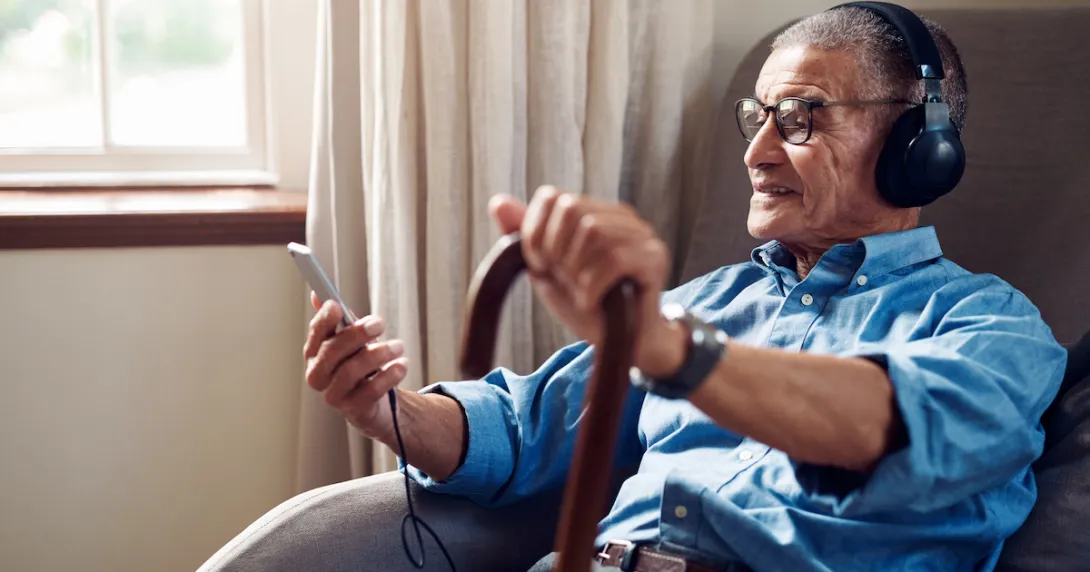 Person sitting in a chair while holding a phone and a cane and wearing headphones Person sitting in a chair while holding a phone and a cane and wearing headphones