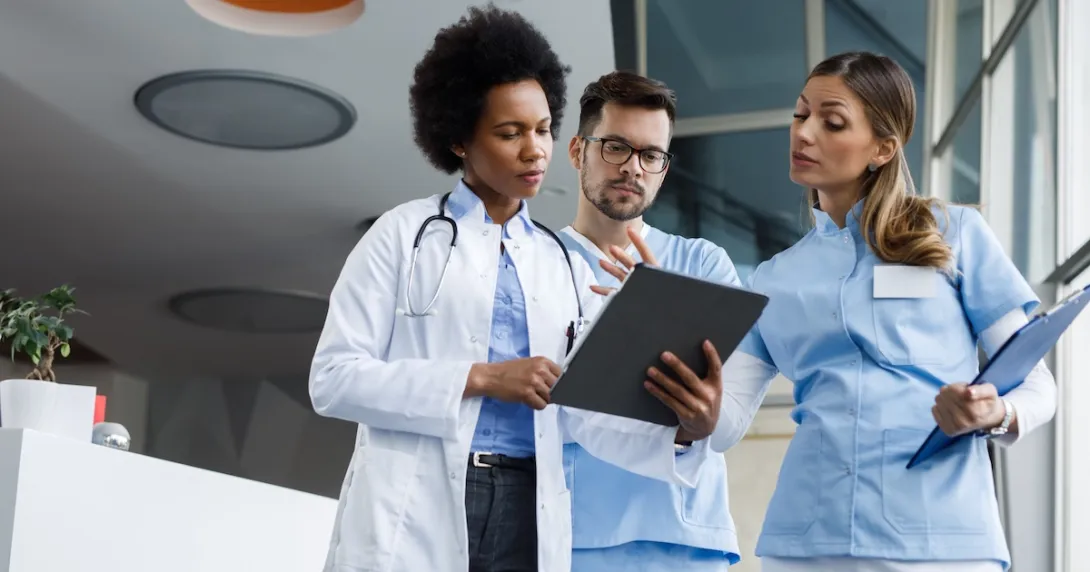 Three healthcare providers standing next to each other and looking at a tablet Three healthcare providers standing next to each other and looking at a tablet