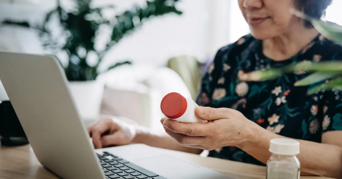 Person on a computer holding medication Person on a computer holding medication