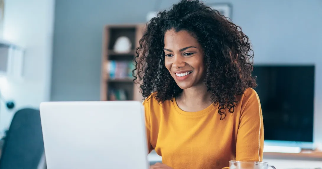 Person sitting in a house looking at a computer and smiling Person sitting in a house looking at a computer and smiling
