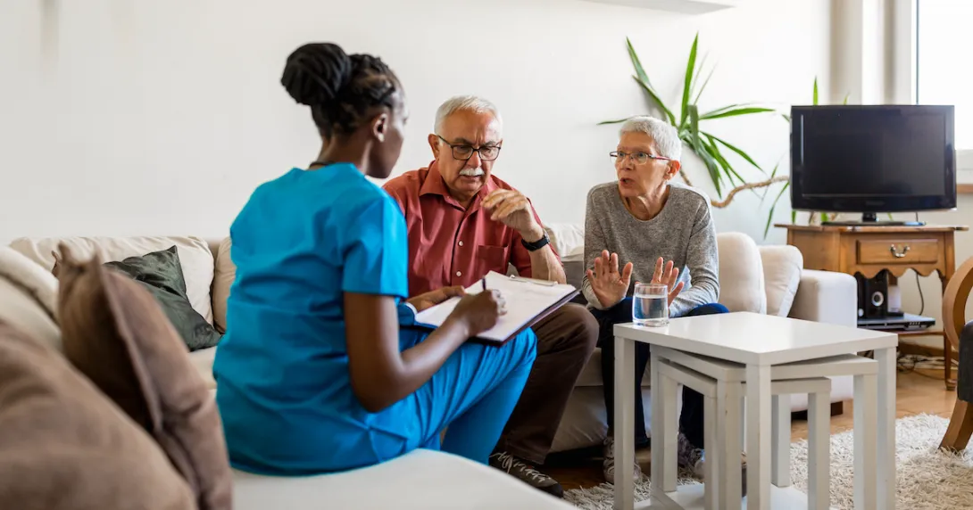 Healthcare provider in scrubs sitting on a couch in a living room with two people Healthcare provider in scrubs sitting on a couch in a living room with two people