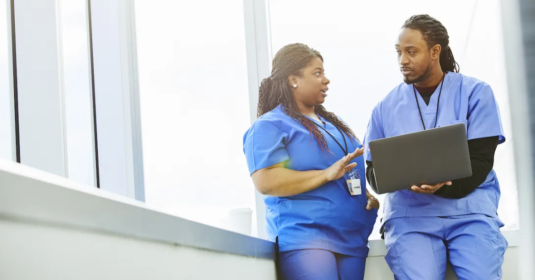 Healthcare providers sitting in by a window while looking at a computer Healthcare providers sitting in by a window while looking at a computer