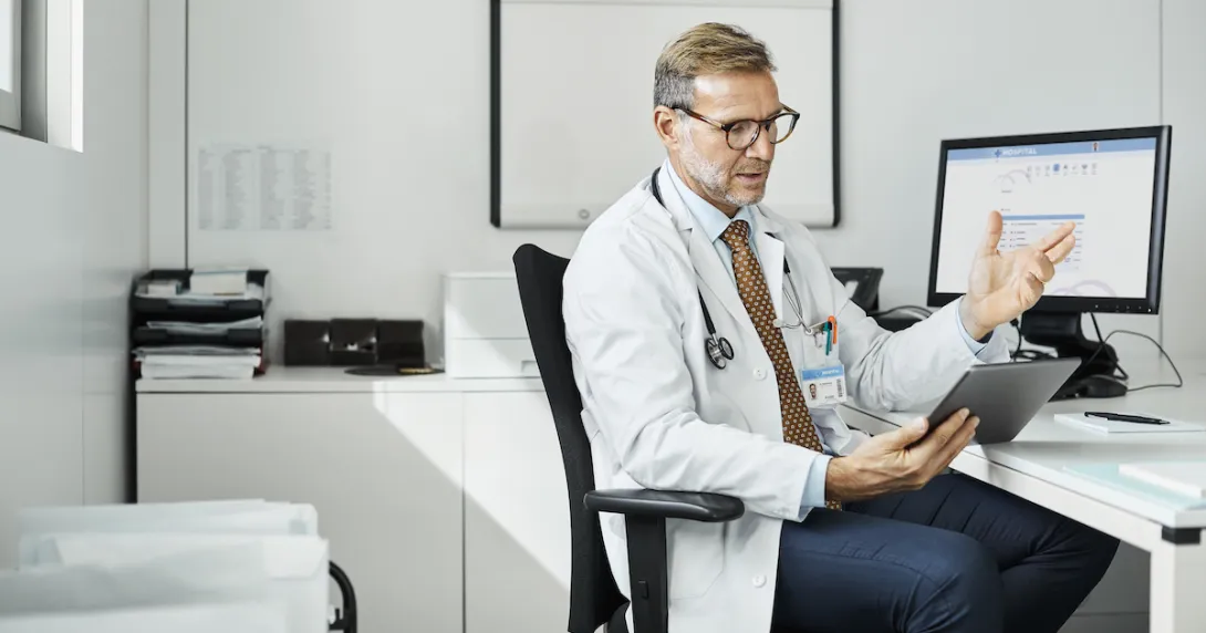 Healthcare provider sitting at a desk while talking to someone on the computer Healthcare provider sitting at a desk while talking to someone on the computer
