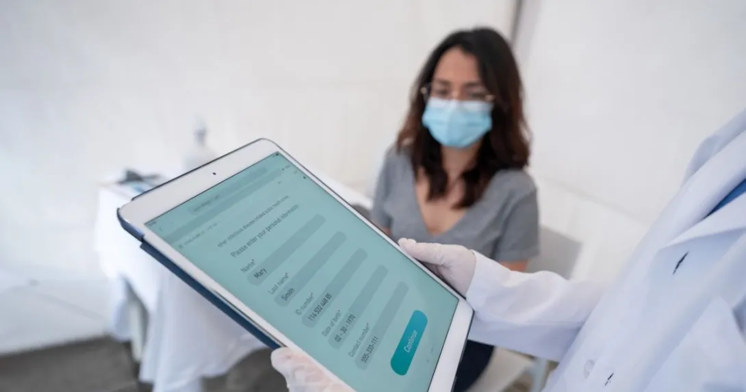 Person holding tablet in front of person wearing surigical mask Person holding tablet in front of person wearing surgical mask
