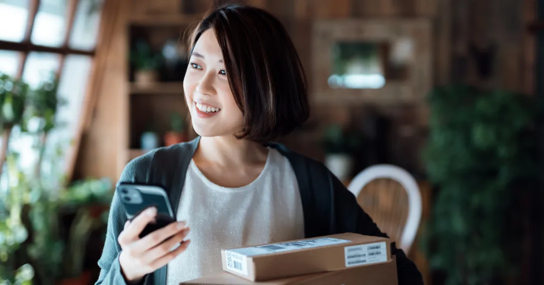 Person smiling while in their home and holding a phone with boxes around them Person smiling while in their home and holding a phone with boxes around them
