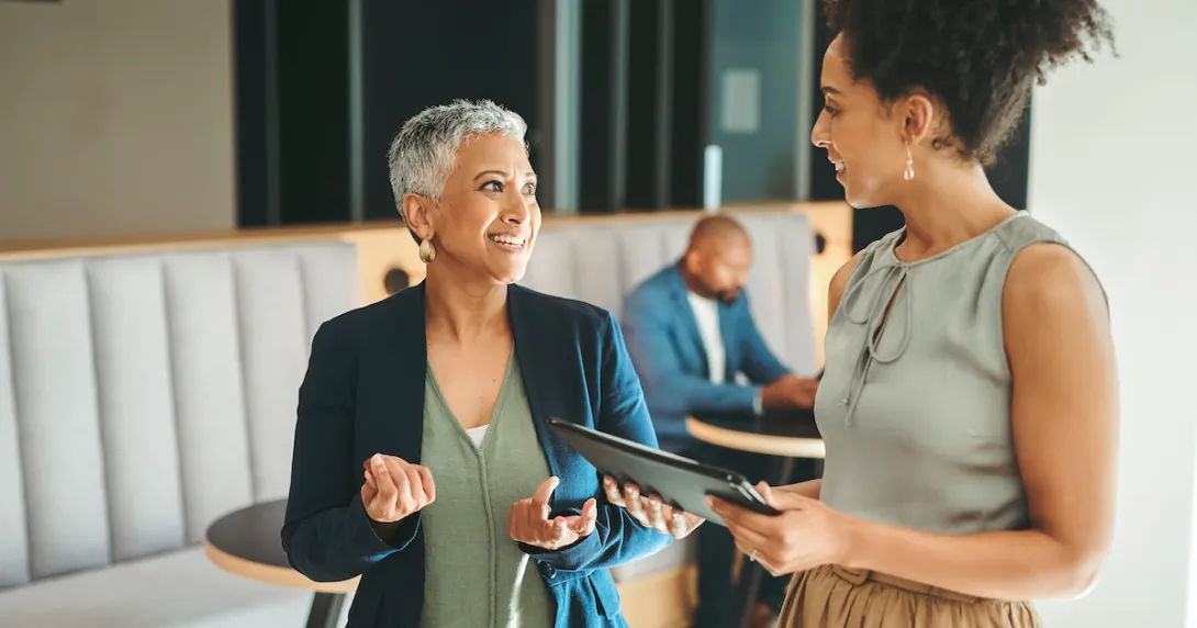 Two individuals walking in an office while another one is sitting in the background Two individuals walking in an office while another one is sitting in the background