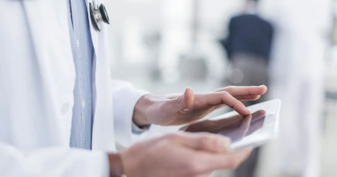Healthcare provider wearing a lab coat with a stethoscope around their neck while holding a tablet Healthcare provider wearing a lab coat with a stethoscope around their neck while holding a tablet