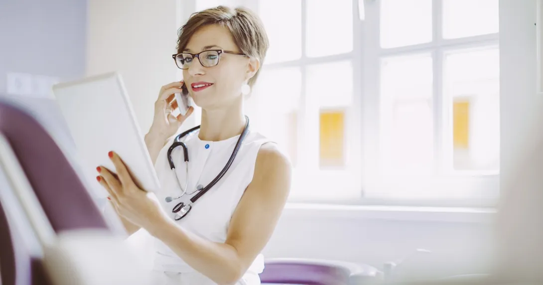 Healthcare provider sitting down in a clinicak setting while looking at a tablet Healthcare provider sitting down in a clinicak setting while looking at a tablet