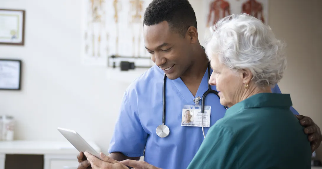 Healthcare provider and a patient standing next to each other both looking at a tablet Healthcare provider and a patient standing next to each other both looking at a tablet