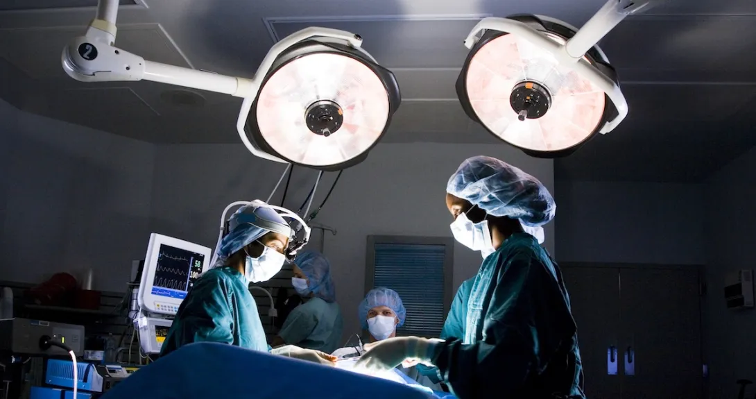 Healthcare providers performing surgery on a patient with lights shining down from the ceiling Healthcare providers performing surgery on a patient with lights shining down from the ceiling