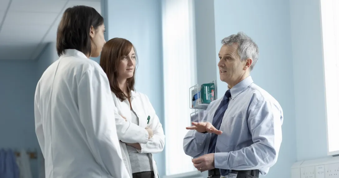 Three healthcare professionals standing in a clinical setting Three healthcare professionals standing in a clinical setting