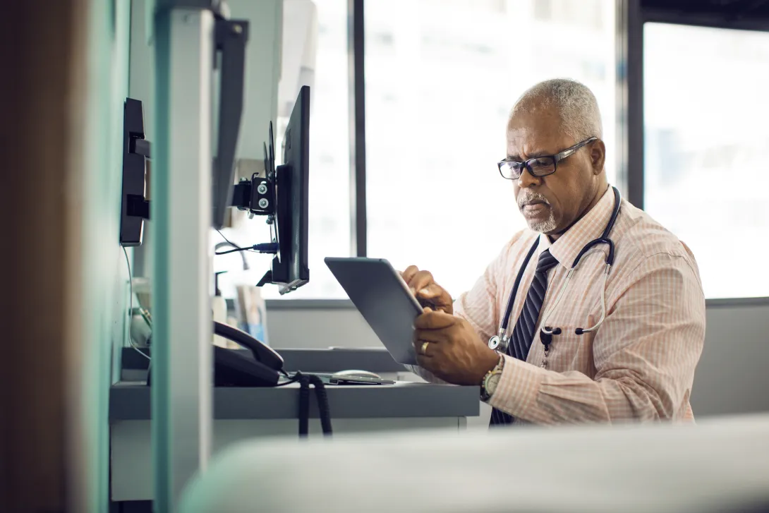 Healthcare provider sitting at a desk while looking at a tablet Healthcare provider sitting at a desk while looking at a tablet