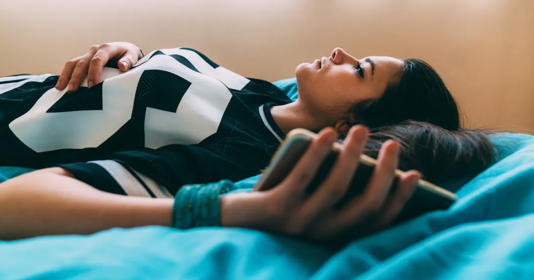 Person lying on a bed looking up at the ceiling while holding onto a cellphone Person lying on a bed looking up at the ceiling while holding onto a cellphone