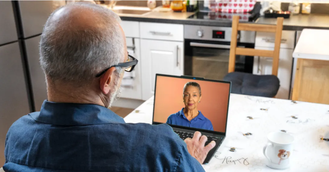 Person sitting at a table while looking at a computer with a person on it Person sitting at a table while looking at a computer with a person on it