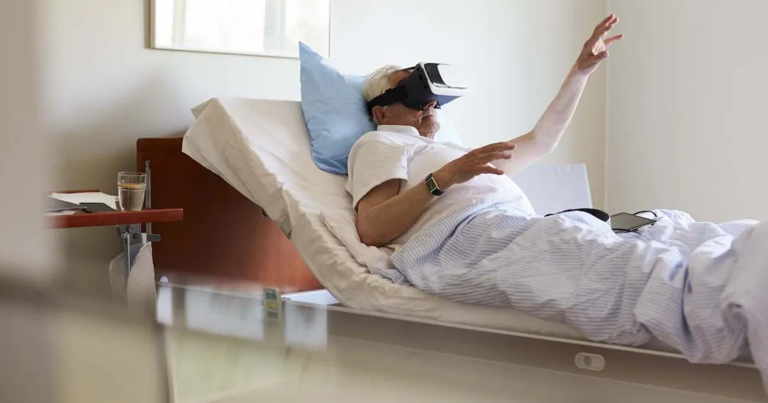 Person in a clinical setting lying in bed with their hand raised while wearing a virtual reality headset Person in a clinical setting lying in bed with their hand raised while wearing a virtual reality headset