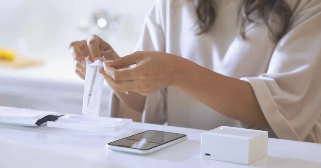 A woman removing the Cue wand from its package with a smartphone and Reader on the table in front of her A woman removing the Cue wand from its package with a smartphone and Reader on the table in front of her