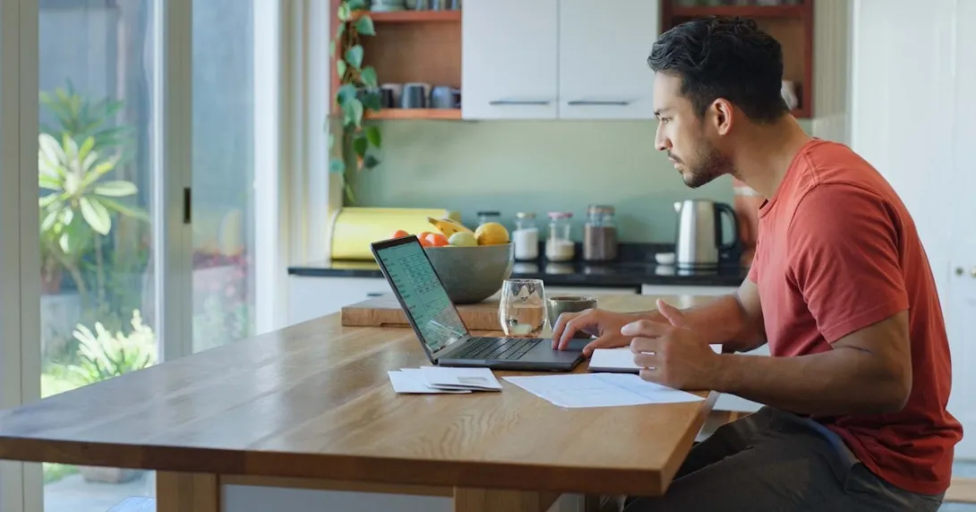 Person sitting at a table in a kitchen looking at their laptop Person sitting at a table in a kitchen looking at their laptop