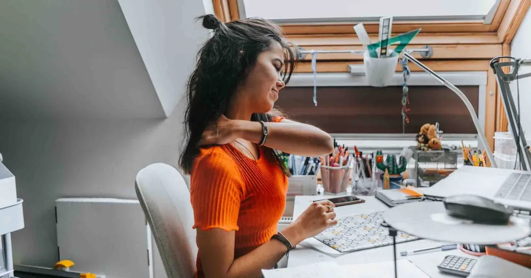 Person rubbing their neck while sitting at a desk Person rubbing their neck while sitting at a desk